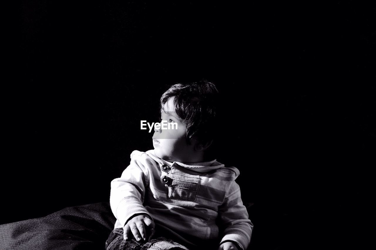 Close-up of cute boy looking away over black background