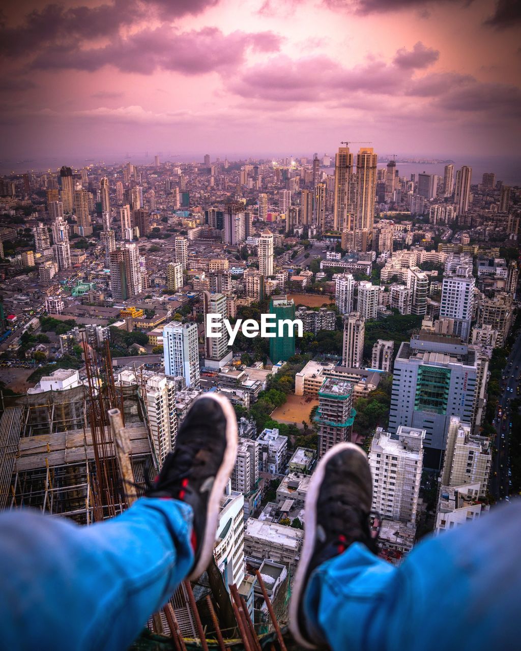 Low section of person sitting above cityscape at sunset