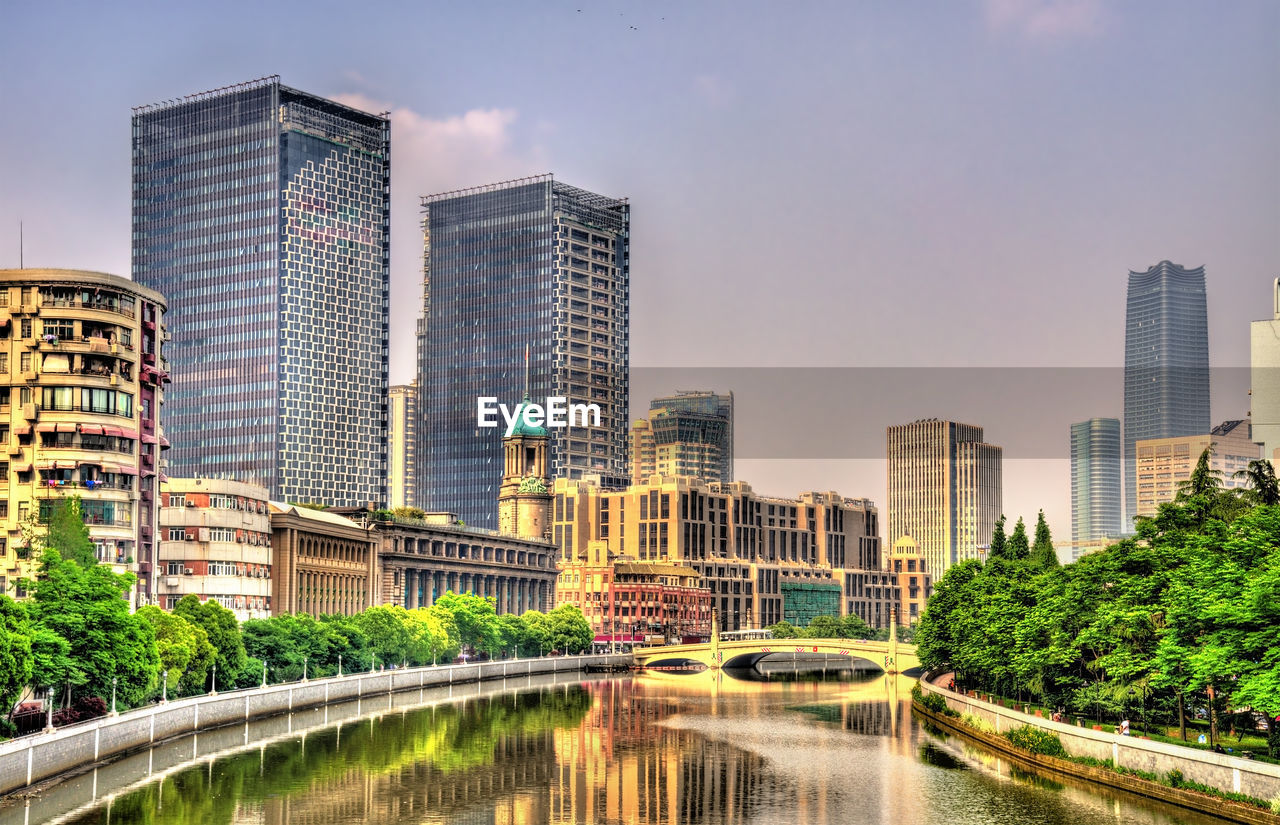 SKYSCRAPERS BY RIVER AGAINST BUILDINGS IN CITY