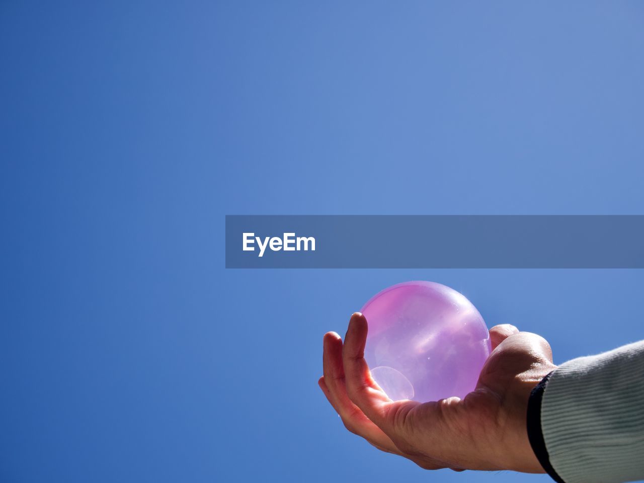 Cropped hand of person holding water balloon against clear blue sky