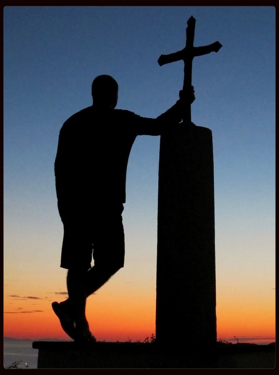 Silhouette man standing by cross during sunset