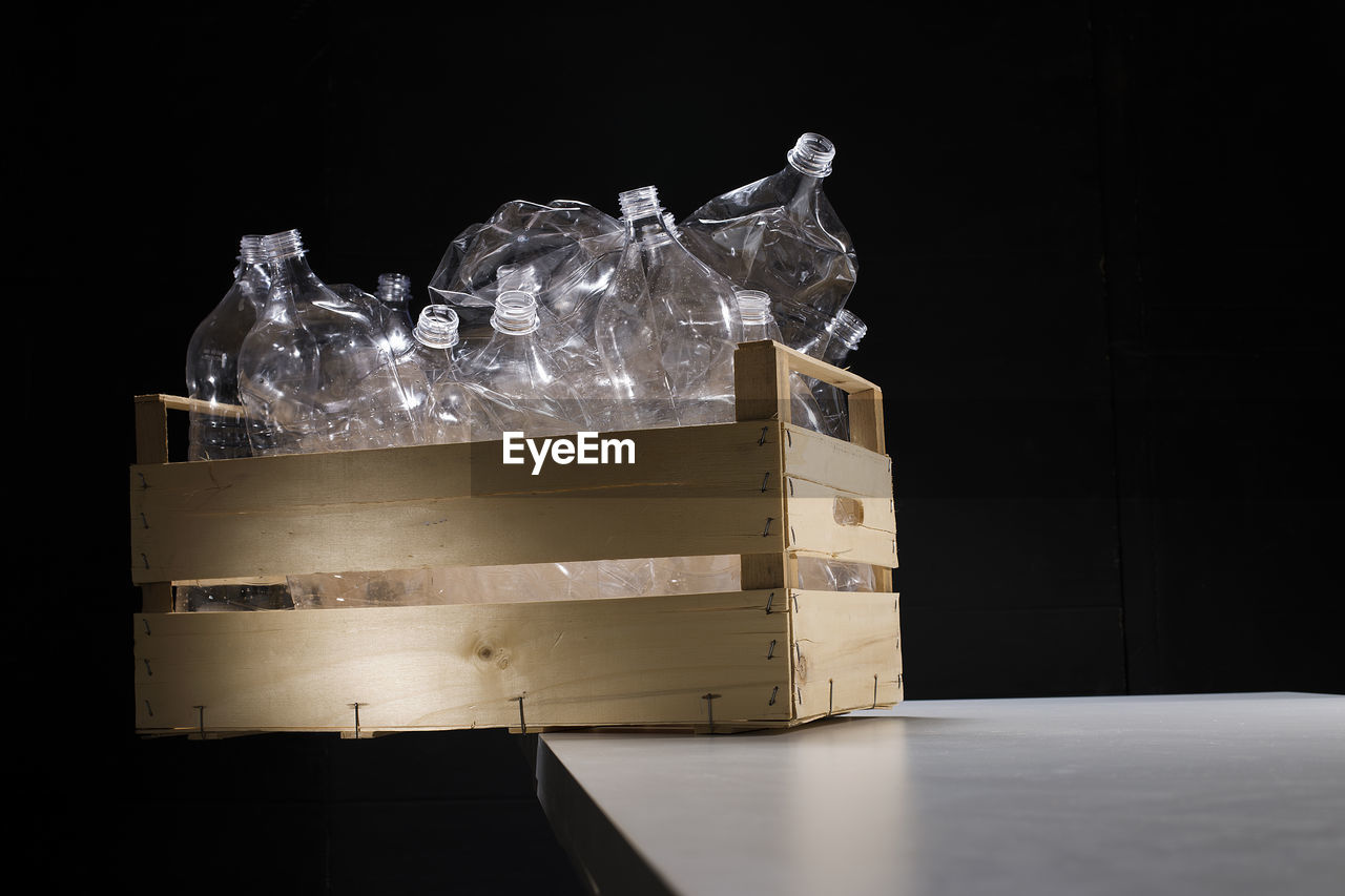Plastic bottles in wooden crate on table against black background