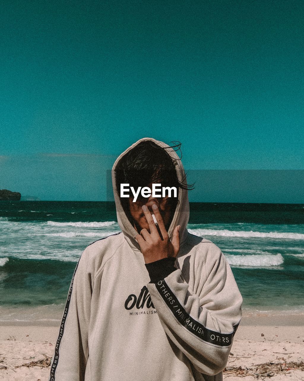 Portrait of young man smoking at beach against clear sky