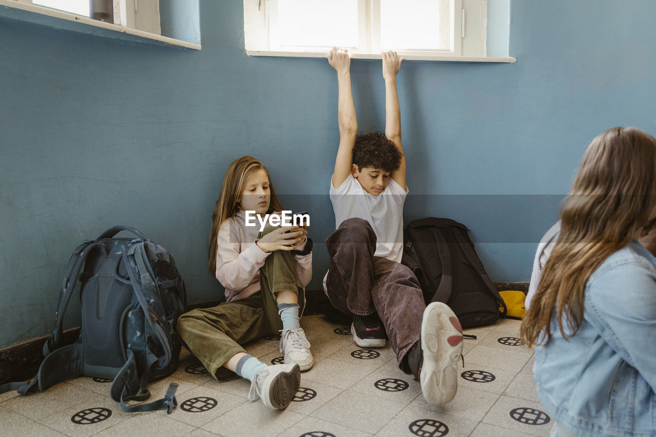 Girl using smart phone sitting by male friend stretching while sitting in school