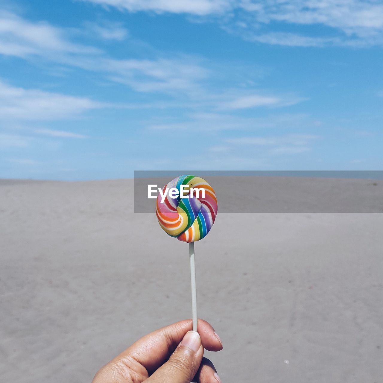 Cropped image of hand holding colorful lollipop at beach against sky