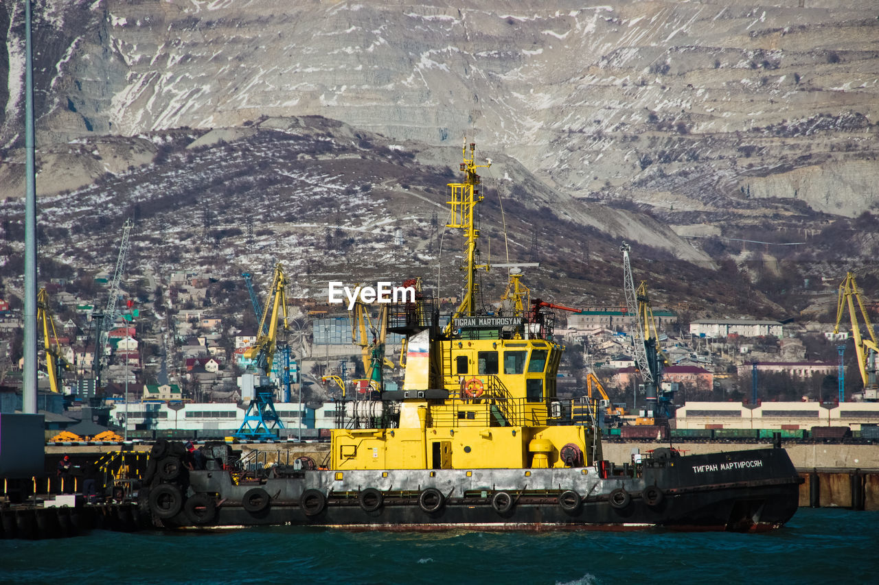 Sailboats on sea by harbor against mountains