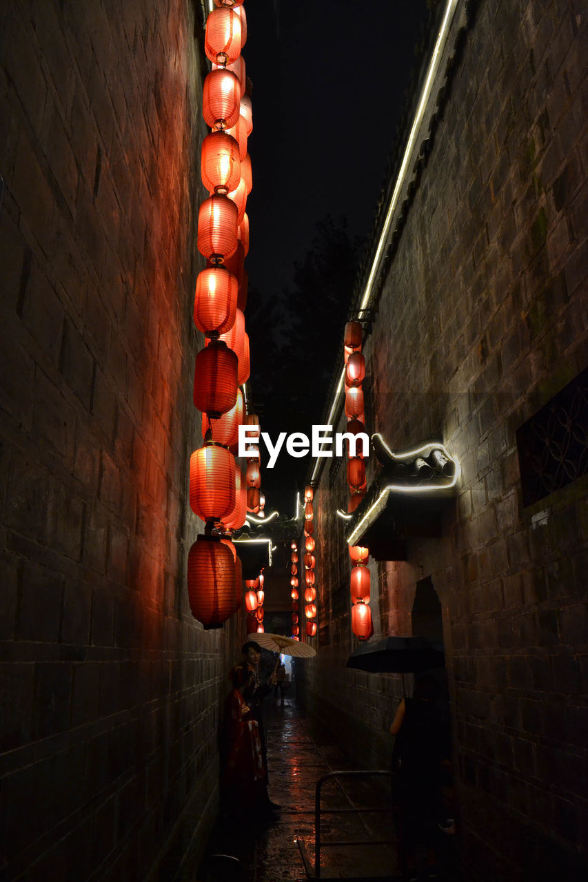 LOW ANGLE VIEW OF ILLUMINATED LIGHTS HANGING FROM WALL IN CITY