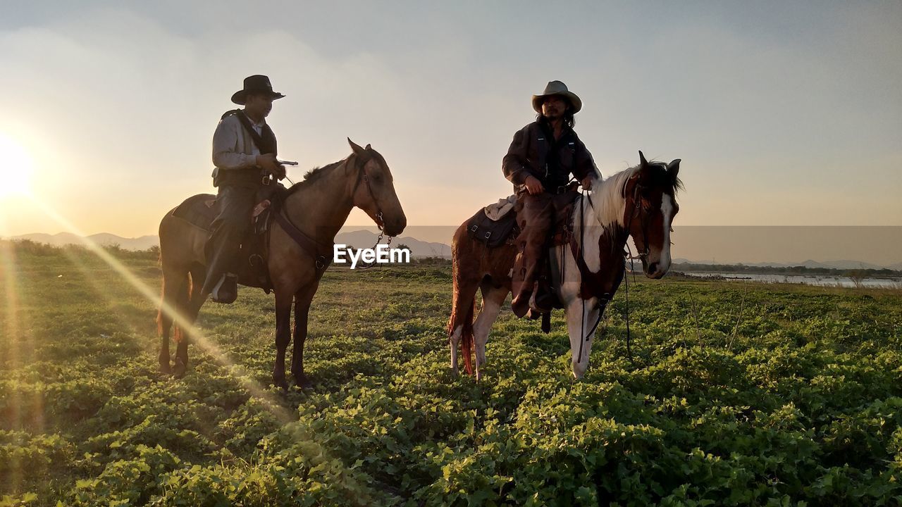 Men riding horses on field against sky