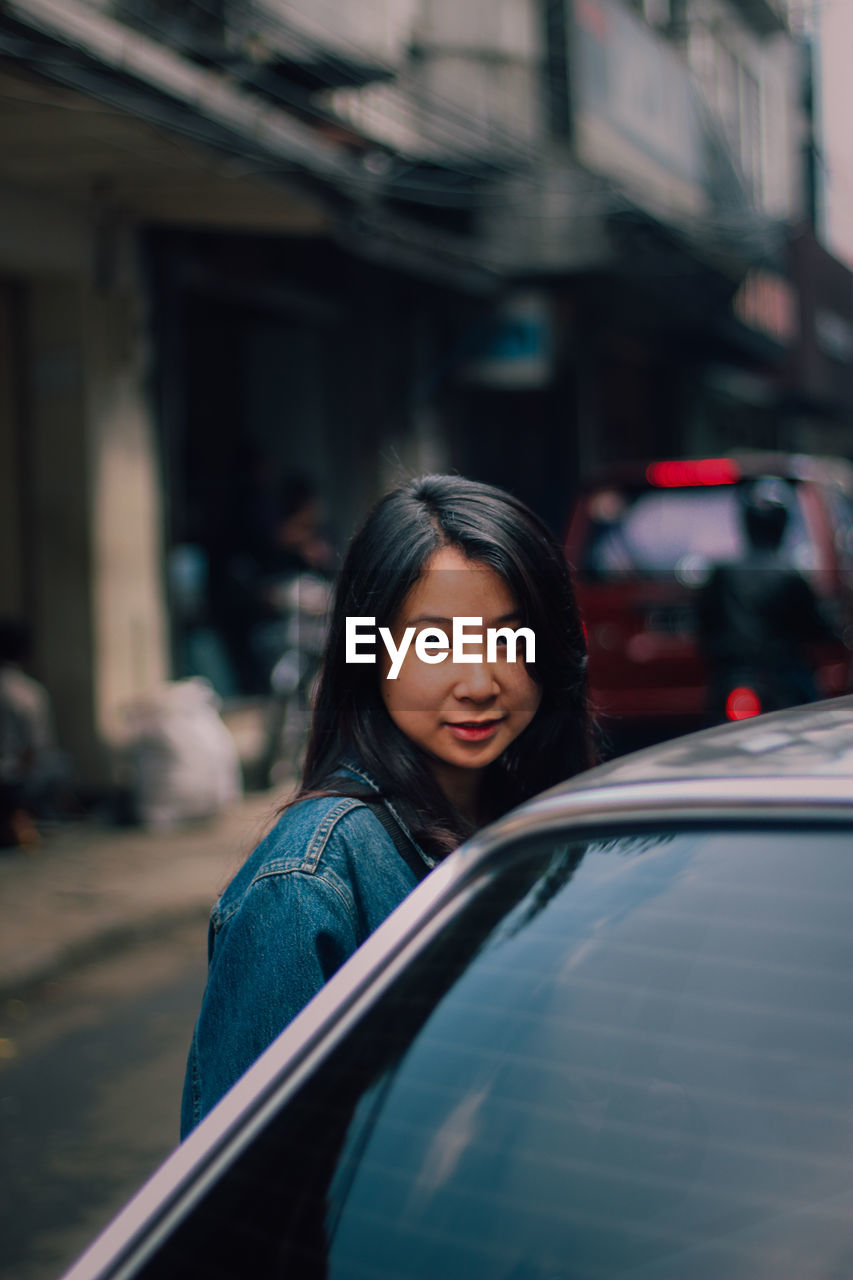 Portrait of young woman by car