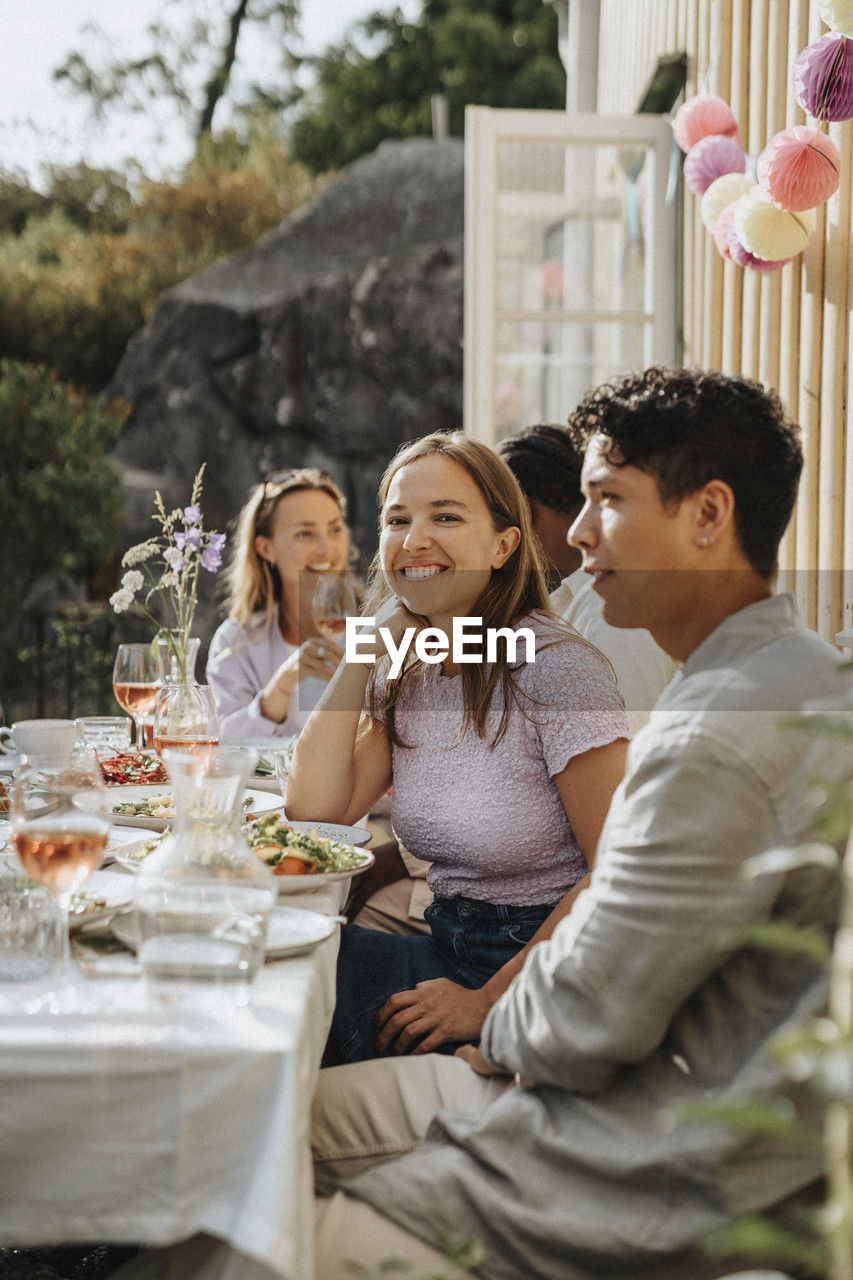 Smiling young man sitting with male friends celebrating dinner party at cafe