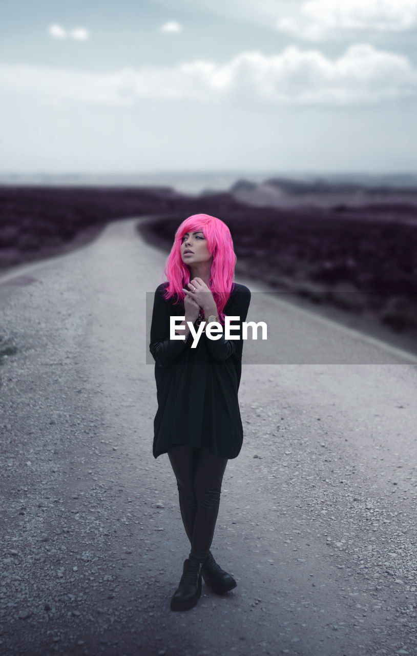 Young woman with dyed hair standing on road against sky