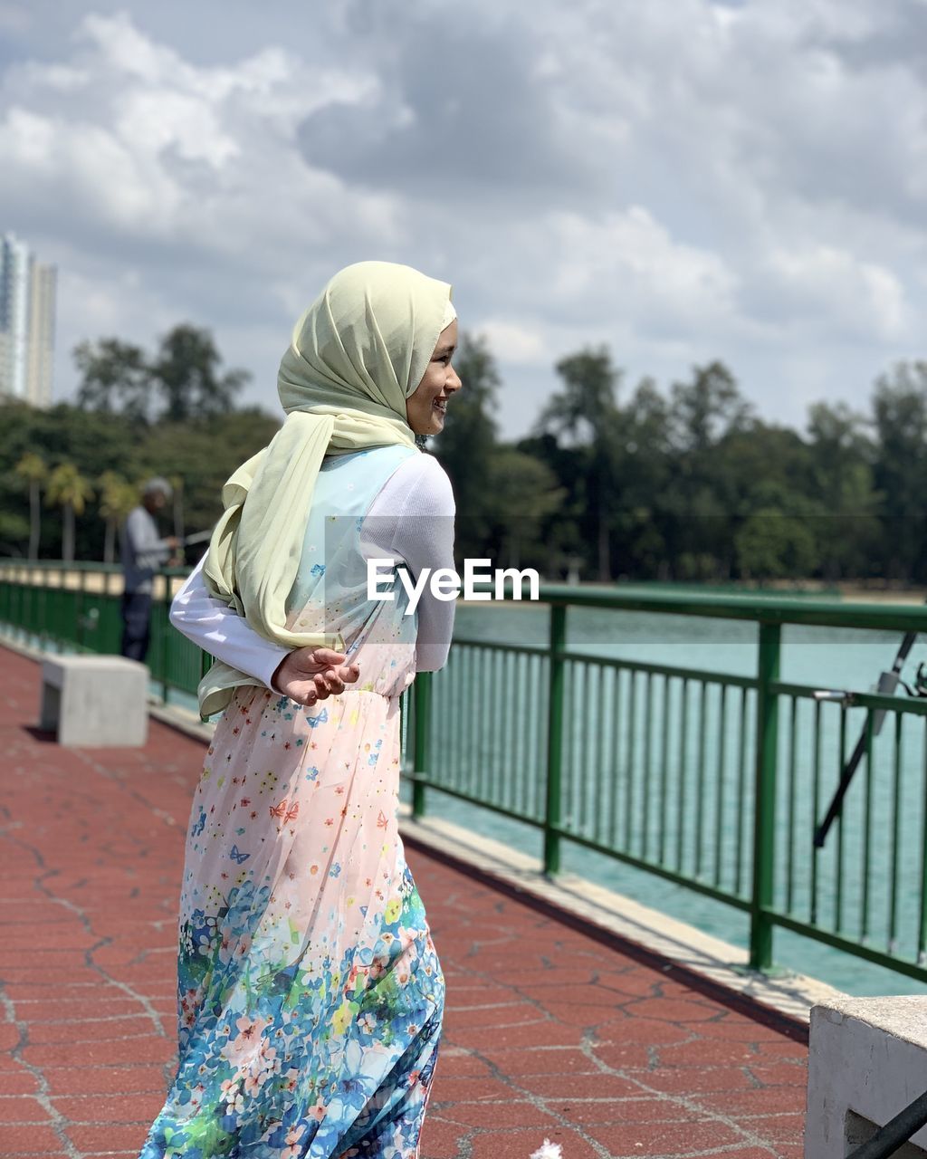 Side view of smiling girl standing by railing against sky