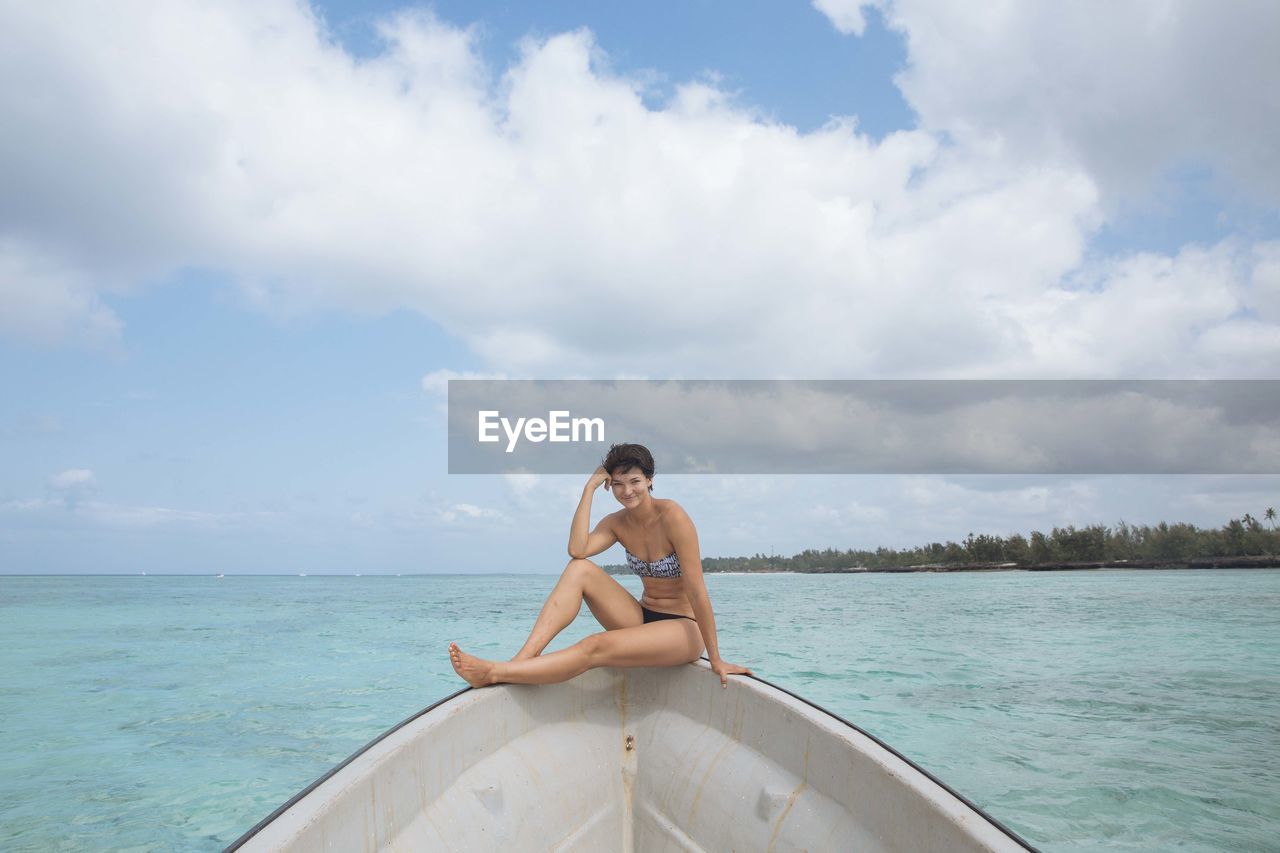 WOMAN SITTING ON SEA AGAINST CLOUDY SKY