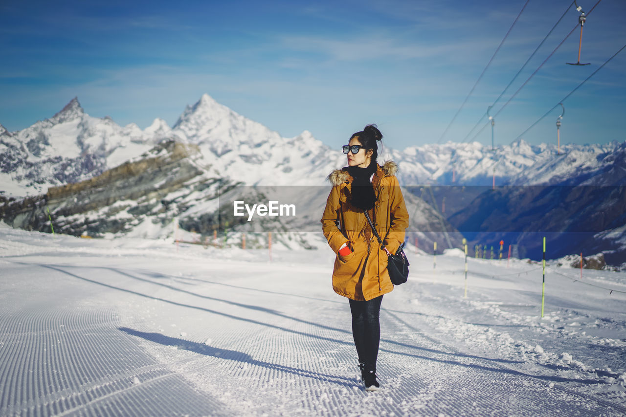 Woman walking on snow covered landscape against sky