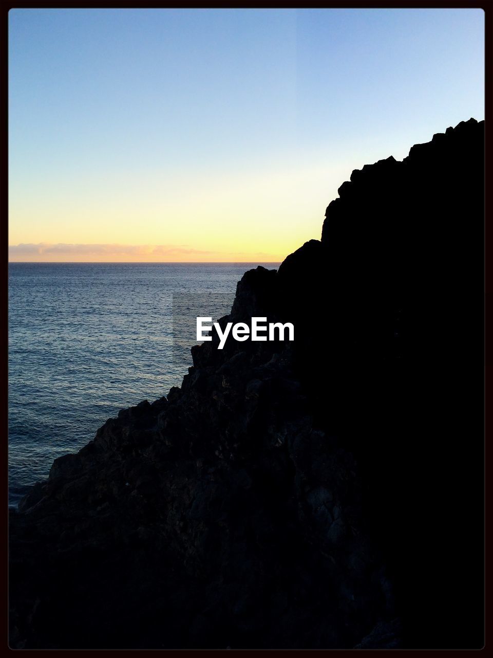 Silhouette mountain by sea against clear sky during sunset