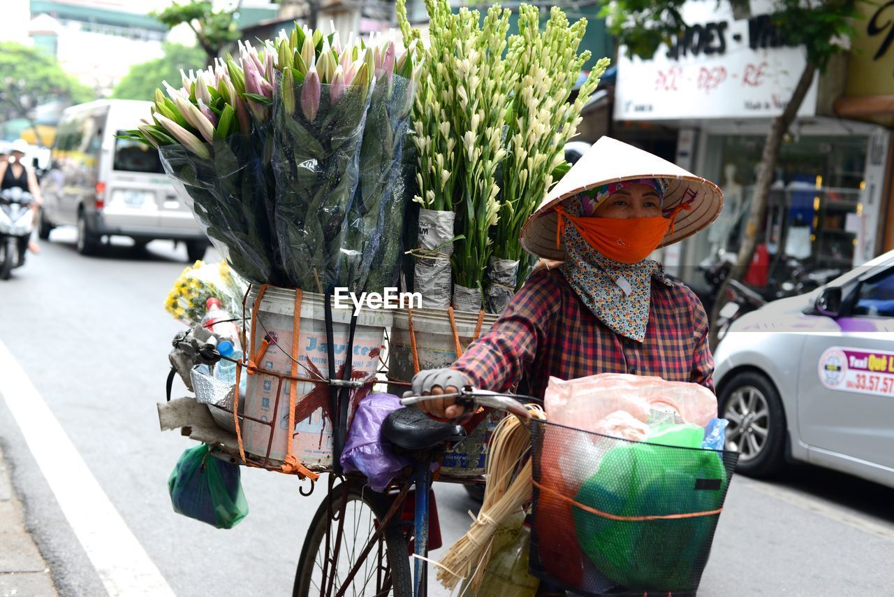 Midsection of woman with bicycle in city selling fresh flowers 