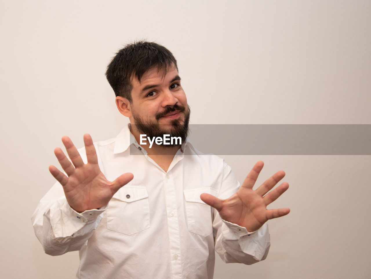one person, gesturing, men, adult, beard, studio shot, facial hair, indoors, portrait, hand, person, sign language, waist up, finger, emotion, young adult, smiling, hand sign, button down shirt, front view, happiness, business, positive emotion, copy space, white, standing, clothing, businessman, looking, looking at camera, cut out, arm, colored background, thumbs up, cheerful, communication, casual clothing