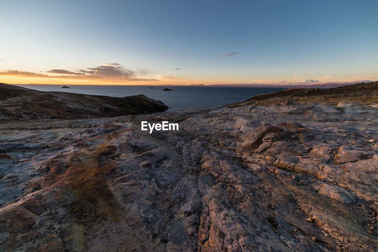 Rocky field by sea against sky during sunset