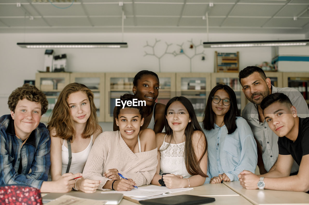 Portrait of professor with teenage students by table in classroom