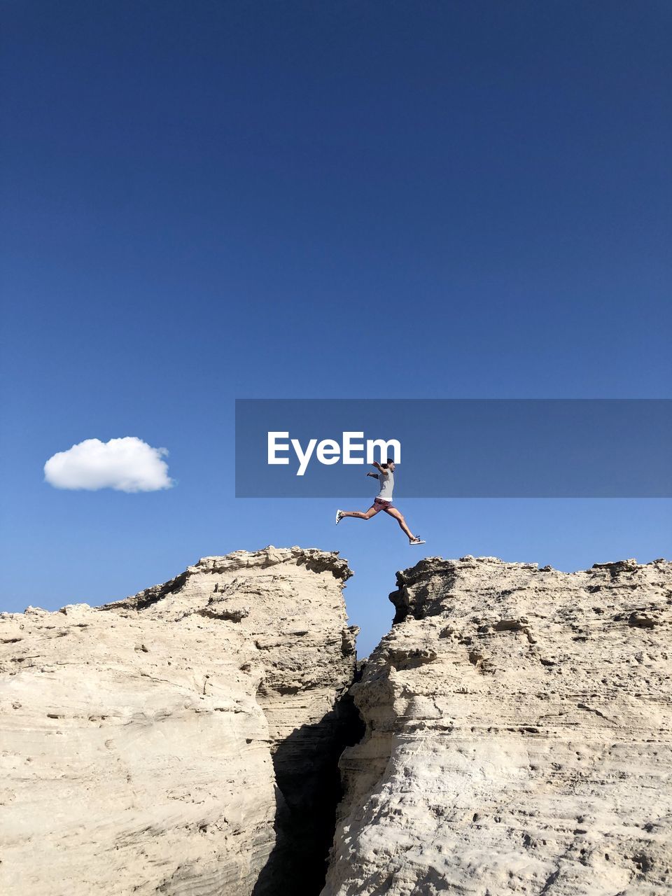 Low angle view of person jumping on rock against blue sky