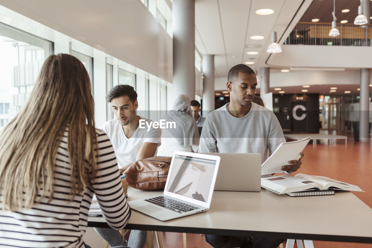 Multi-ethnic students studying together while sitting in university cafeteria