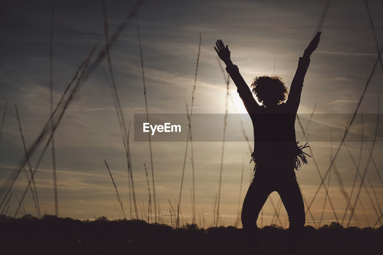 Silhouette carefree woman with arms raised standing on field at sunset