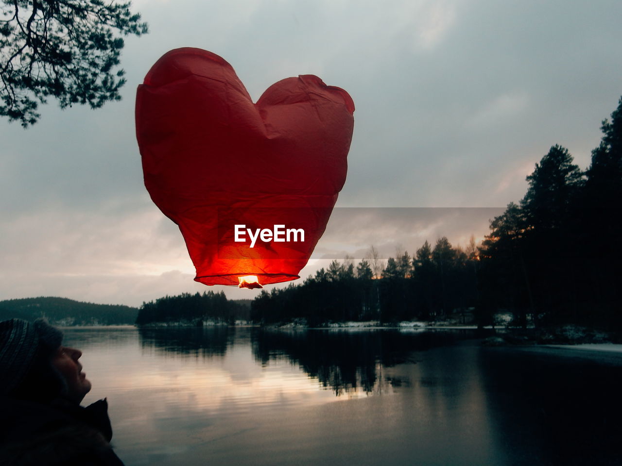 Senior man watching at paper lantern by lake against sky during sunset