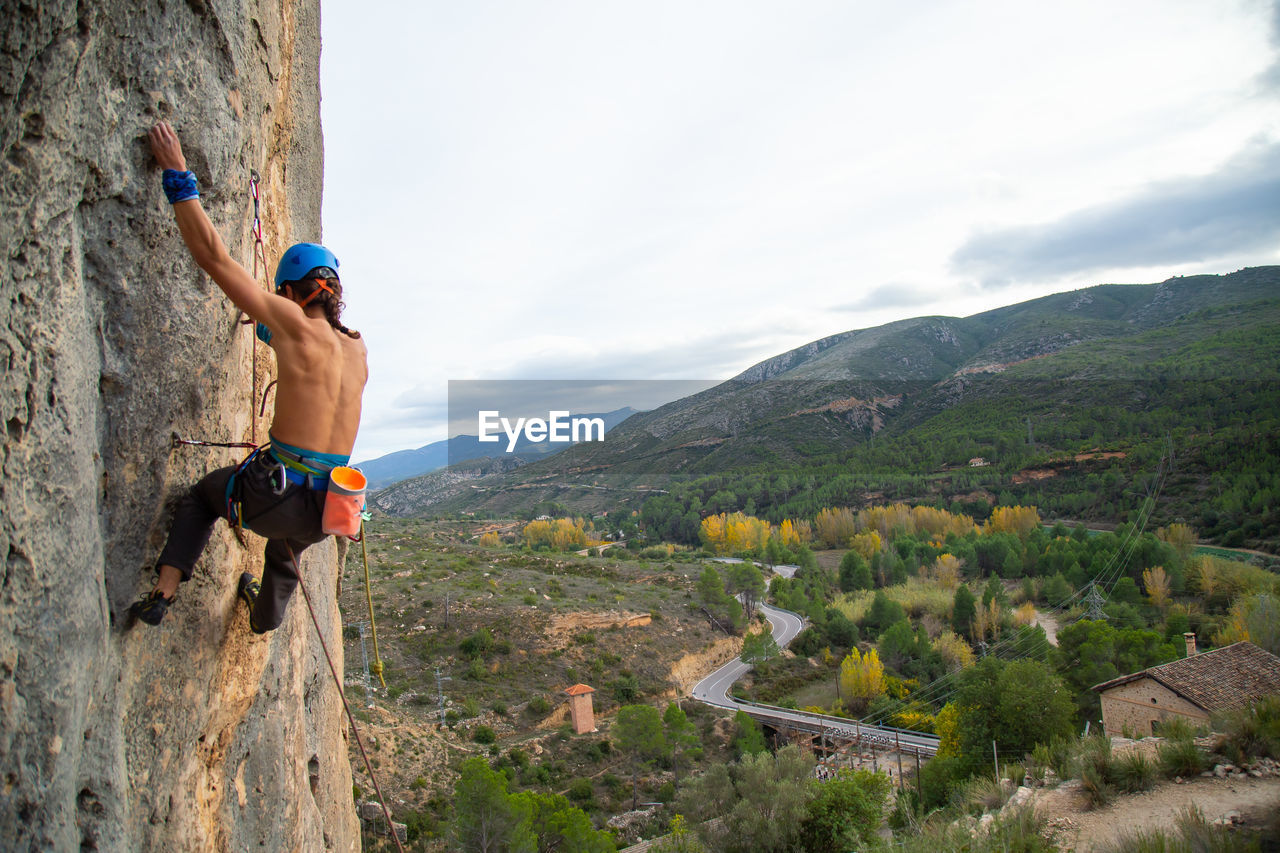 Shirtless man rock climbing against sky