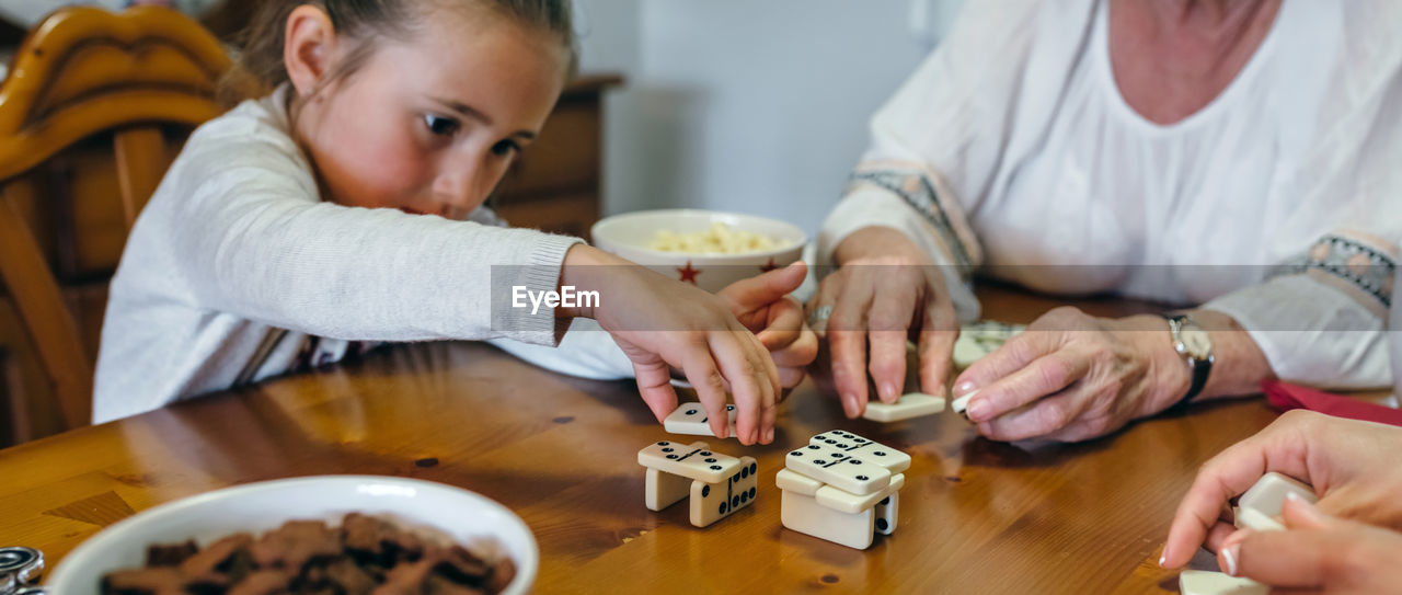 Granddaughter playing domino with grandmother on table at home