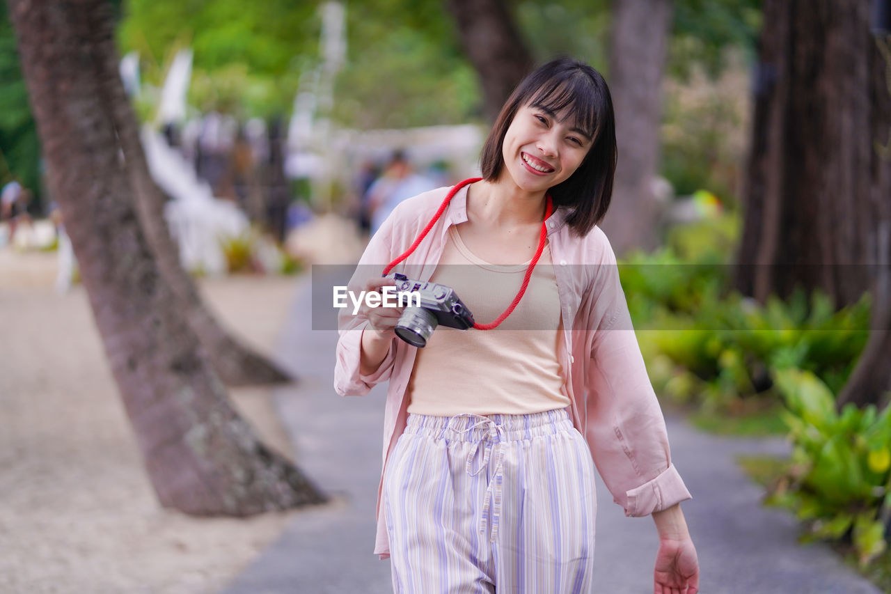 YOUNG WOMAN LOOKING AT CAMERA WHILE STANDING OUTDOORS