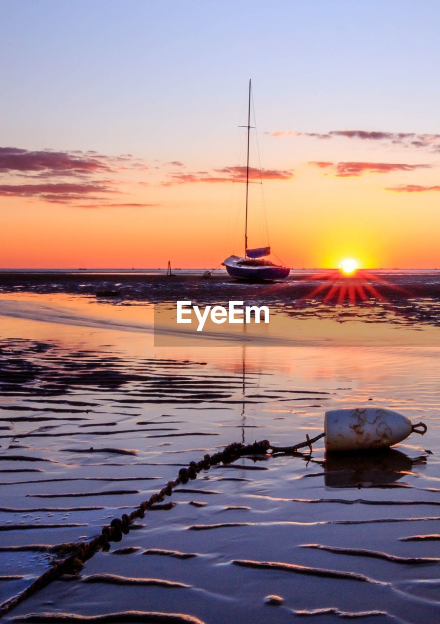 SAILBOATS MOORED ON SEA AGAINST ORANGE SKY