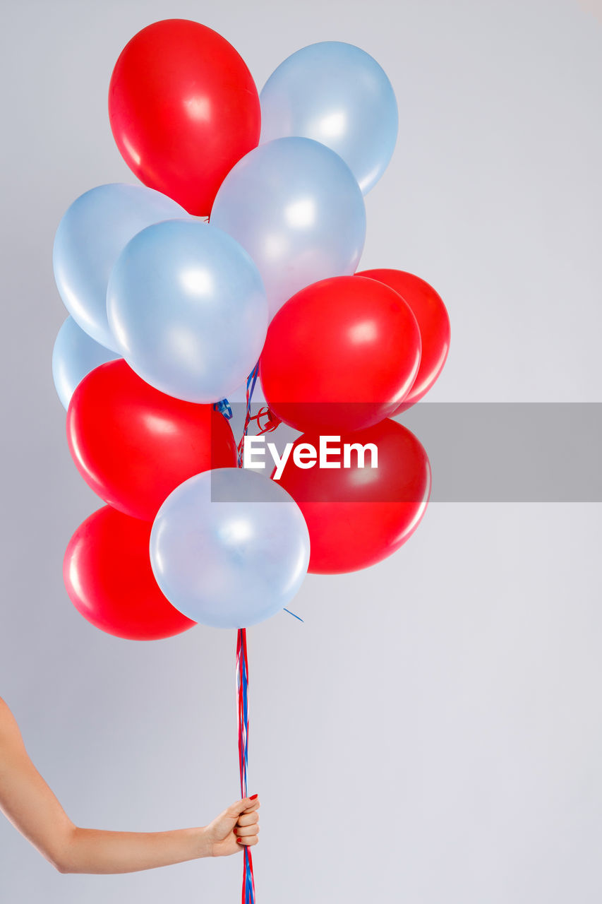 Cropped hand of woman with balloons against white background