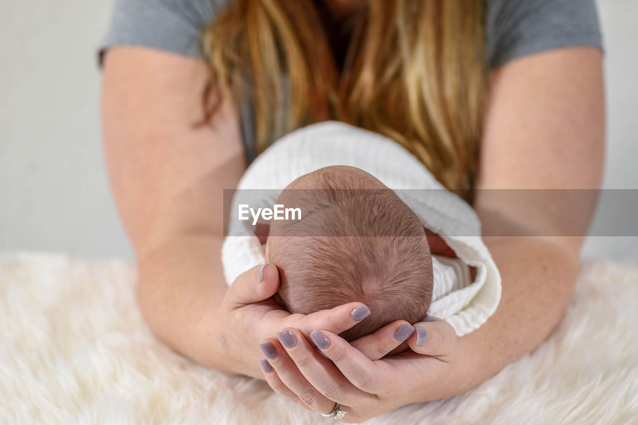 Midsection of mother holding baby boy on bed