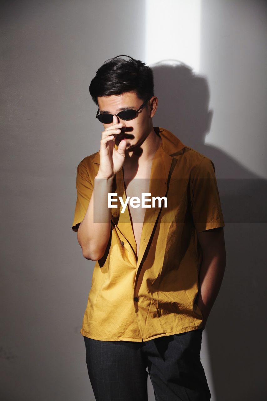 Young man wearing sunglasses standing against wall