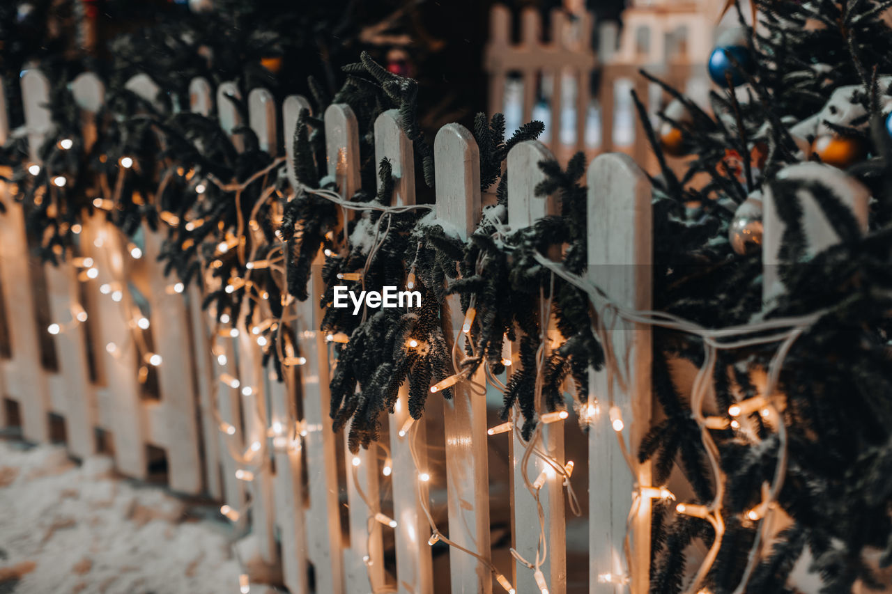 Wooden fence decorated with golden garlands and new year's branches in the snow