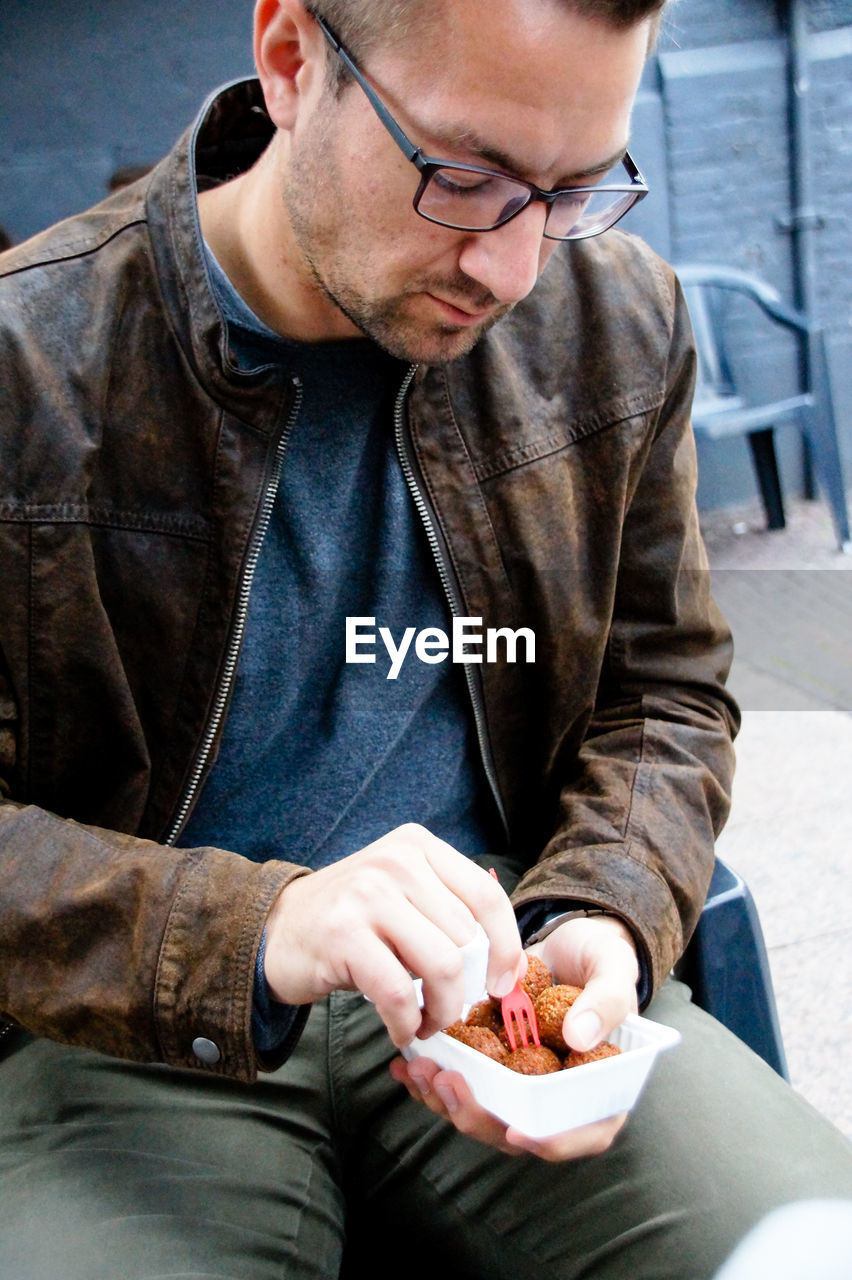 Close-up of man having food while sitting on chair outdoors