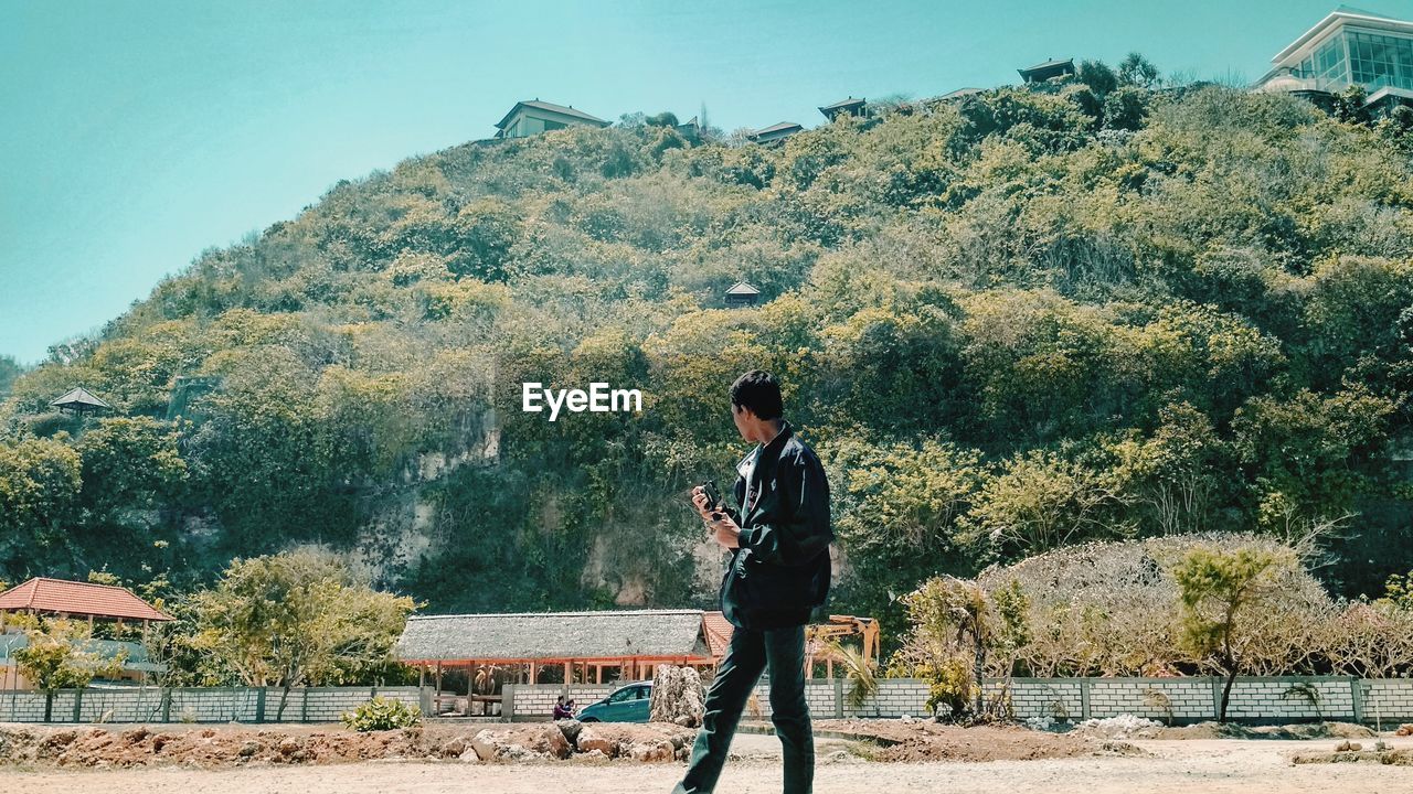 Side view of young man standing on road against mountain during sunny day