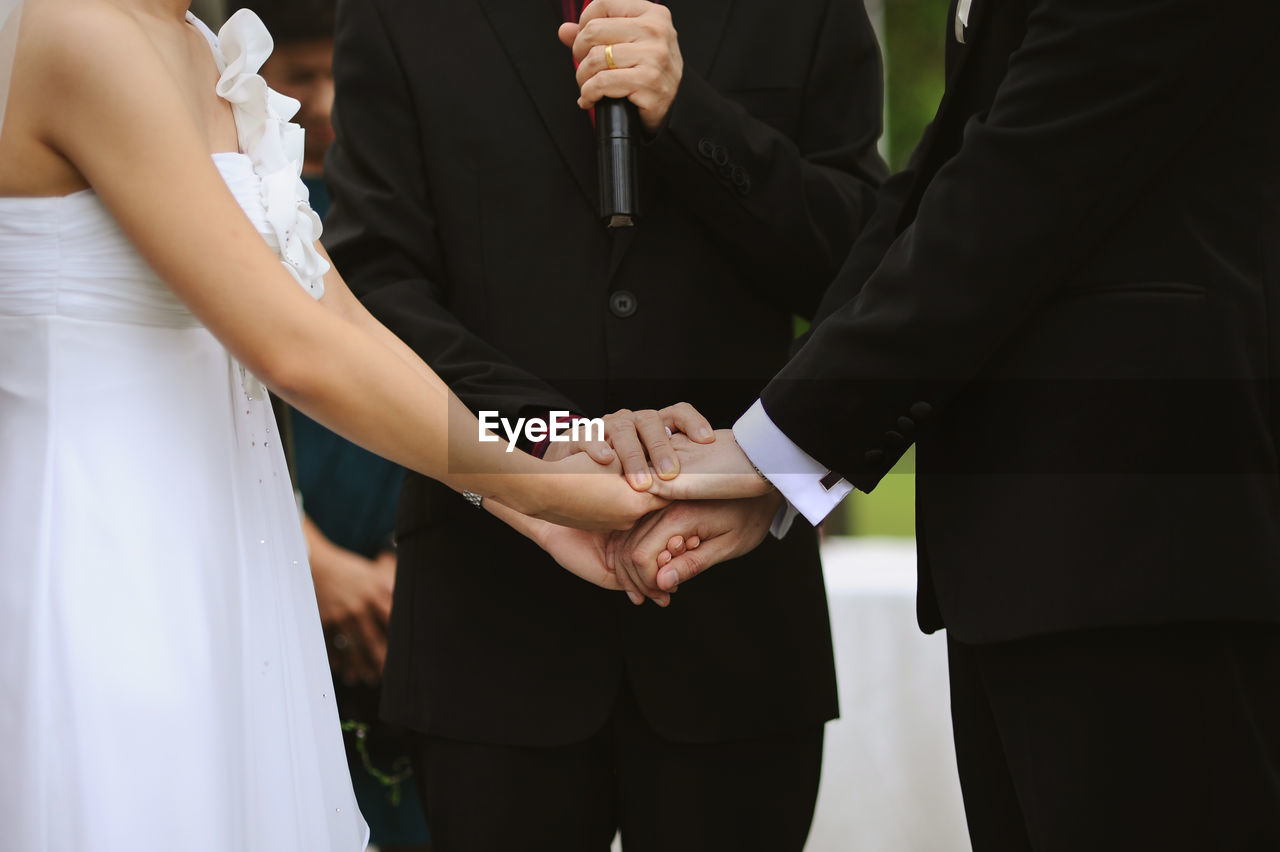 Midsection of priest holding hands of couple during weeding