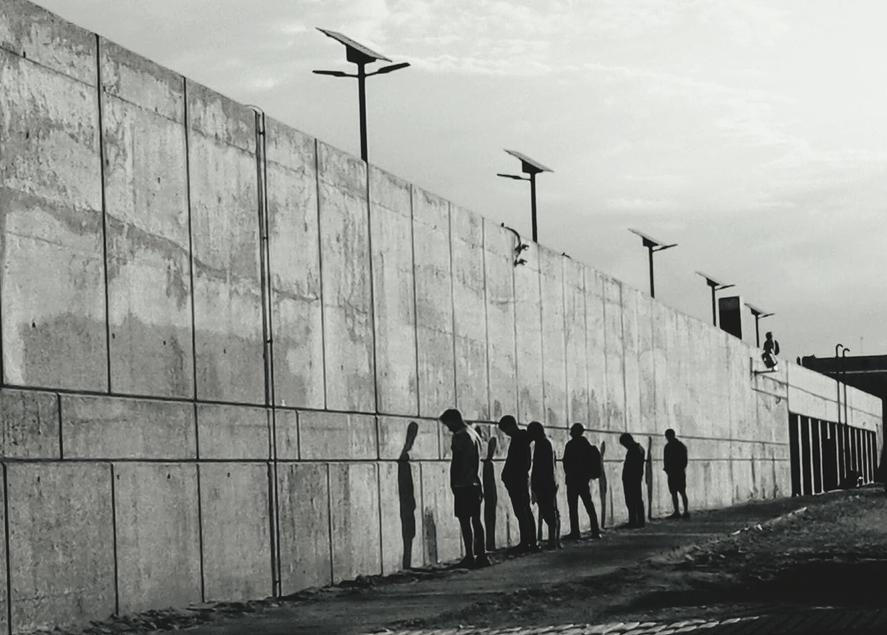 PEOPLE WALKING ON STREET LIGHT AGAINST SKY