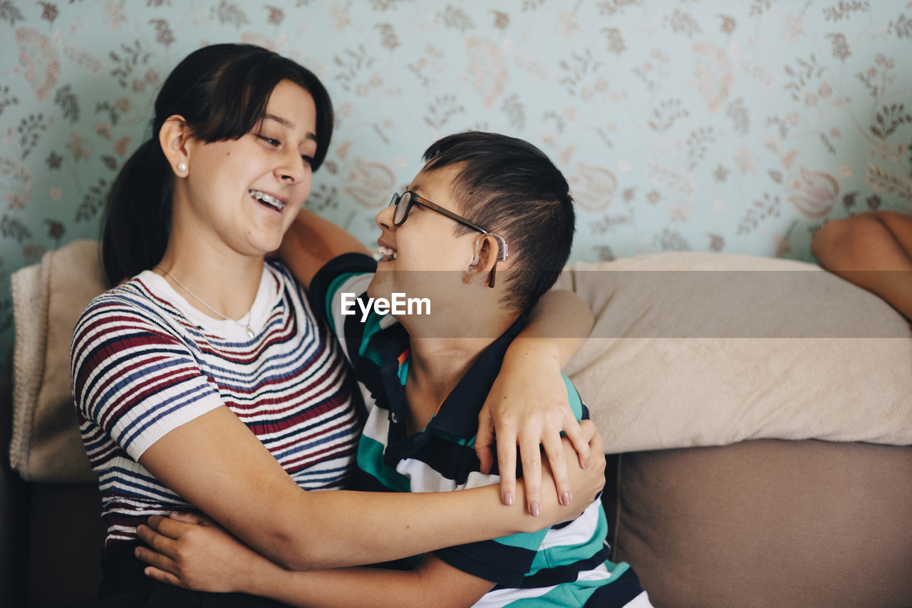 Loving brother and sister embracing on sofa against wall in living room
