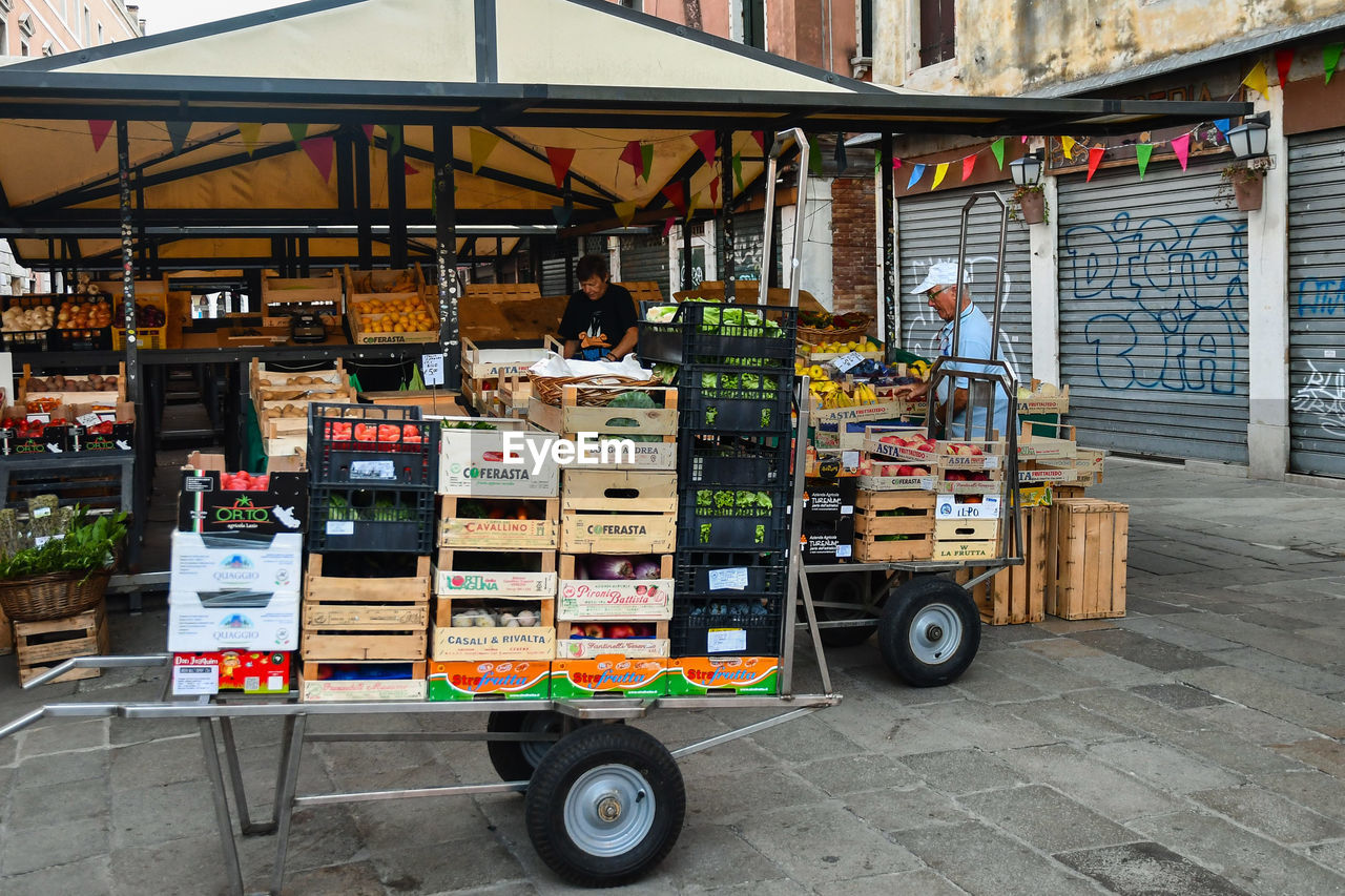 transportation, architecture, city, mode of transportation, business, street, retail, building exterior, market, food and drink, built structure, food, public space, store, vehicle, urban area, day, road, transport, land vehicle, outdoors, travel, building, market stall