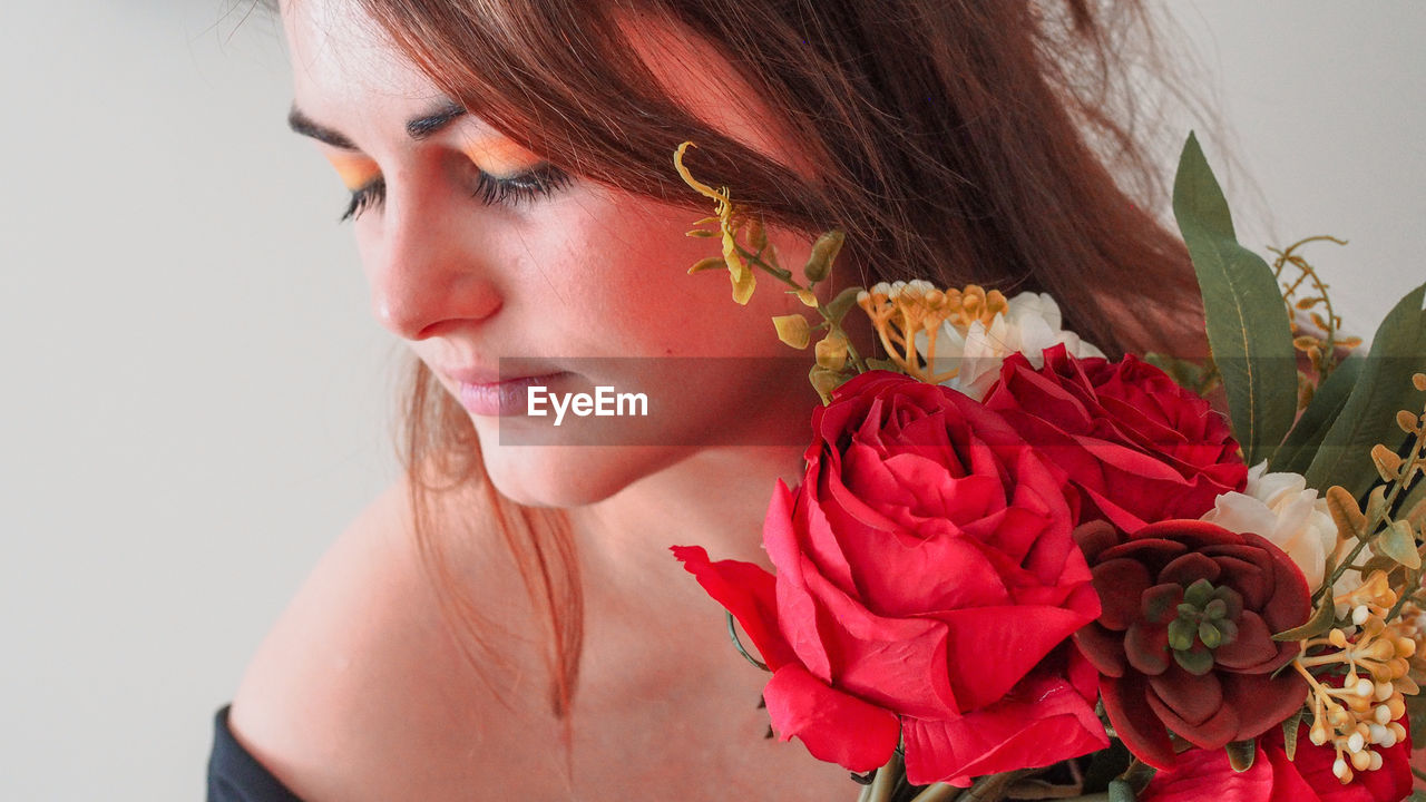 CLOSE-UP OF YOUNG WOMAN HOLDING ROSE AT RED ROSES