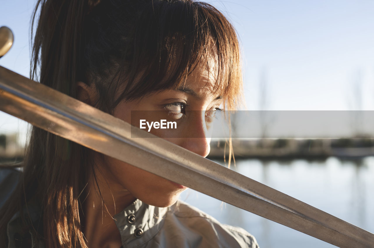 Female athlete with intense look holding sword against her face on sunny day
