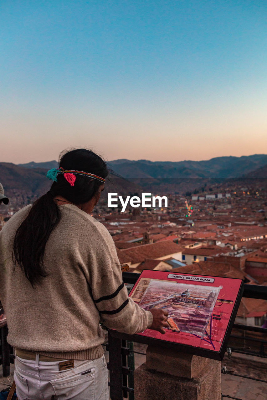 REAR VIEW OF MAN LOOKING AT CITY AGAINST SKY