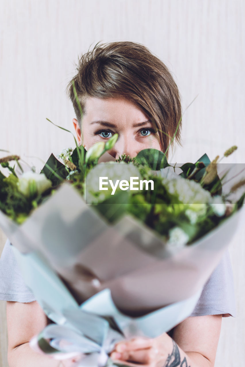 Portrait of woman holding bouquet against wall