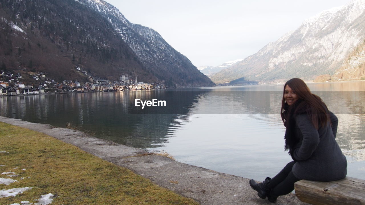 Portrait of woman sitting by lake against mountains