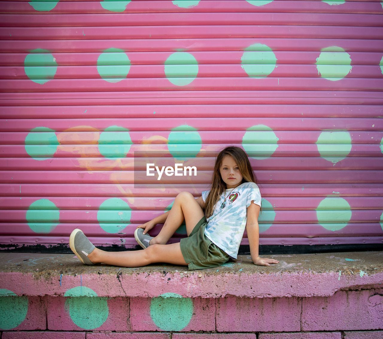 Full length portrait of girl leaning against shutter