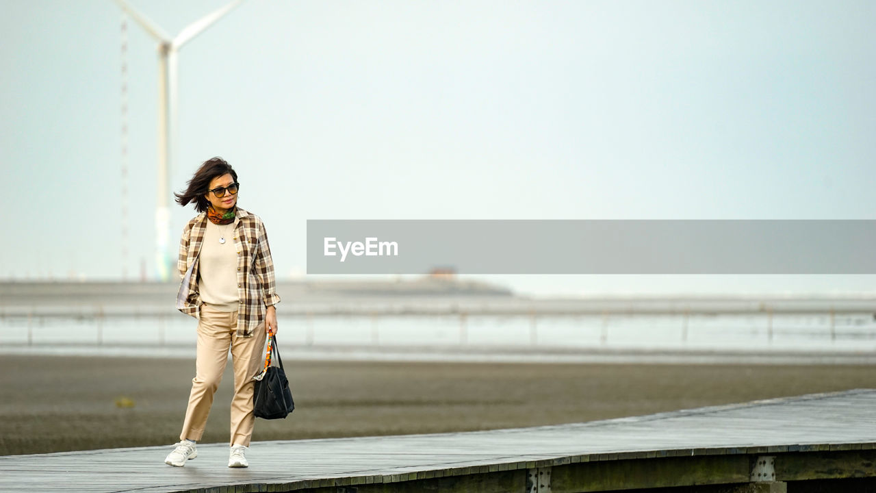 Portrait of young woman standing against railing against sky