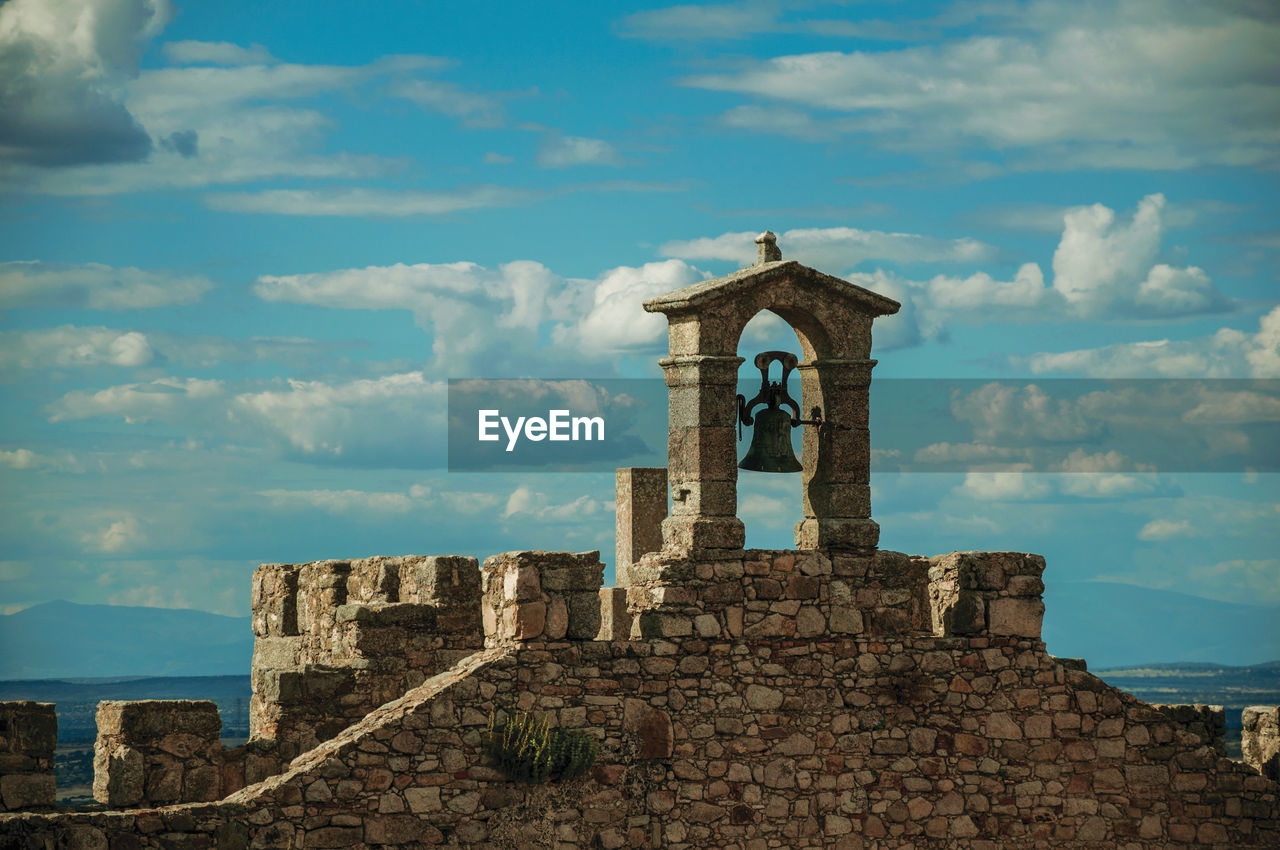 Bell on top of thick stone wall with crenels and merlons at the castle of trujillo. spain.