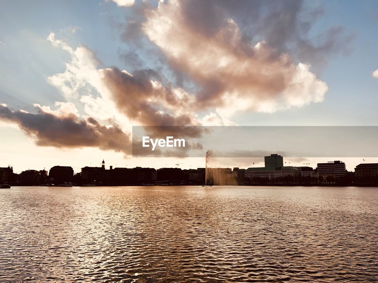 Silhouette buildings by river against sky during sunset